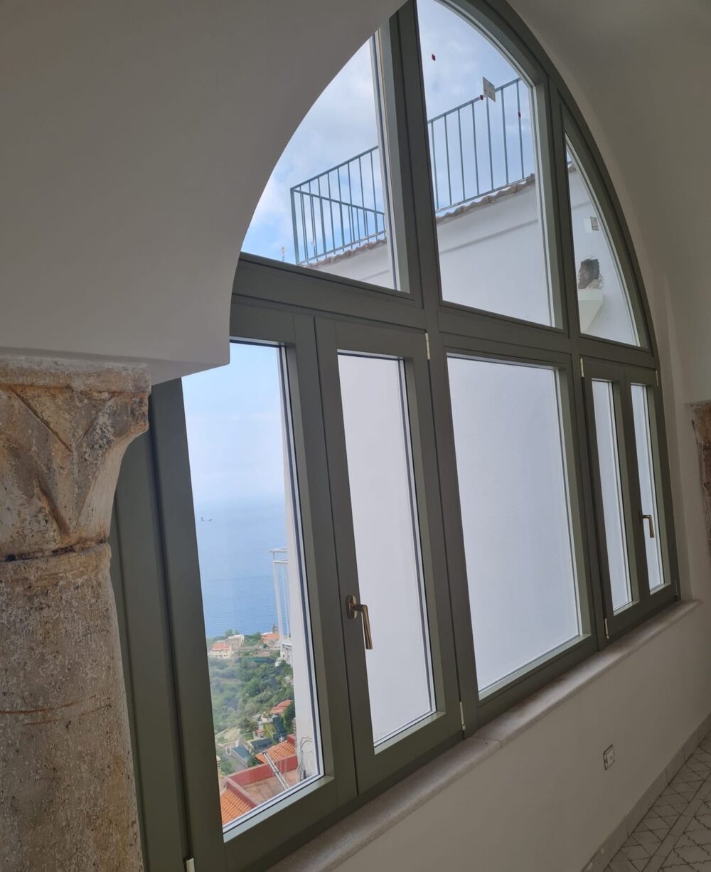 Finestra ad arco in legno con vetrata e colonna in pietra, vista sul golfo