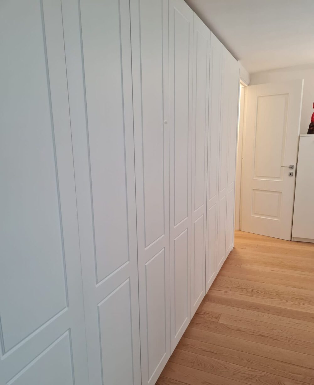 Armadiatura bianca a tutta altezza con ante a specchiature e parquet in rovere