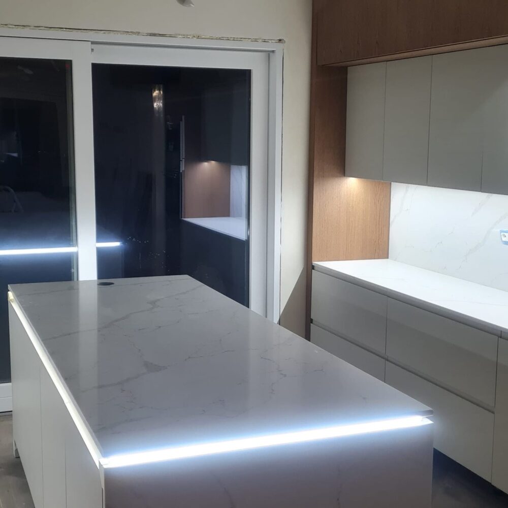 Cucina con isola in marmo bianco illuminata a LED e colonne laccate
