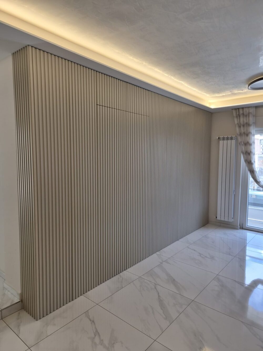 Parete attrezzata con boiserie a listelli, illuminazione a LED a soffitto e pavimento in marmo