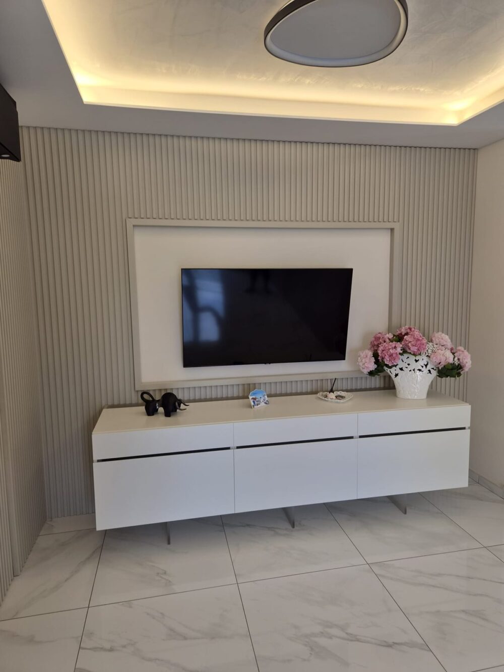 Soggiorno con boiserie a listelli, mobile TV sospeso bianco e controsoffitto illuminato