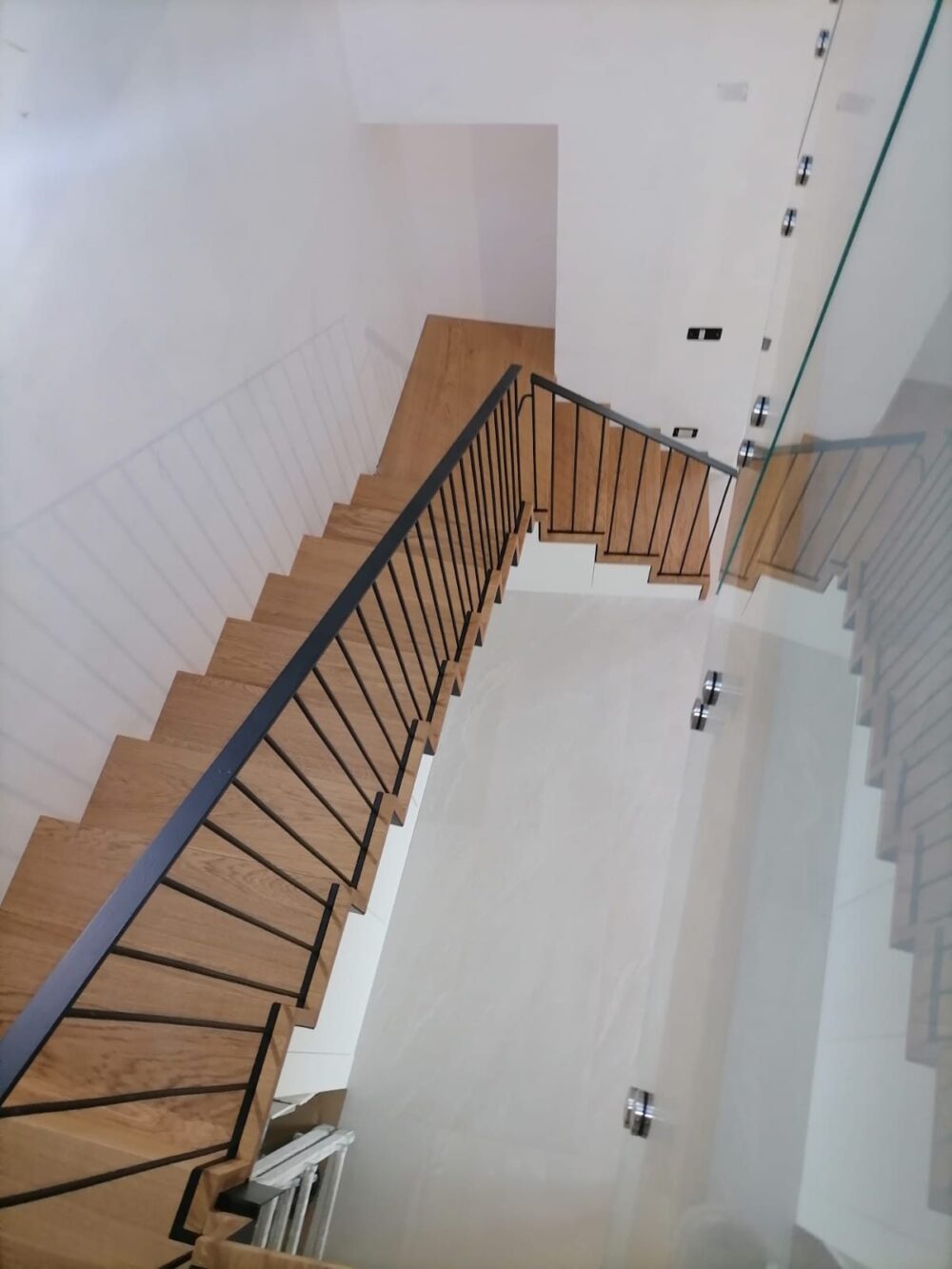Scala in legno di rovere con ringhiera in ferro nero e parapetto in vetro, vista dall'alto
